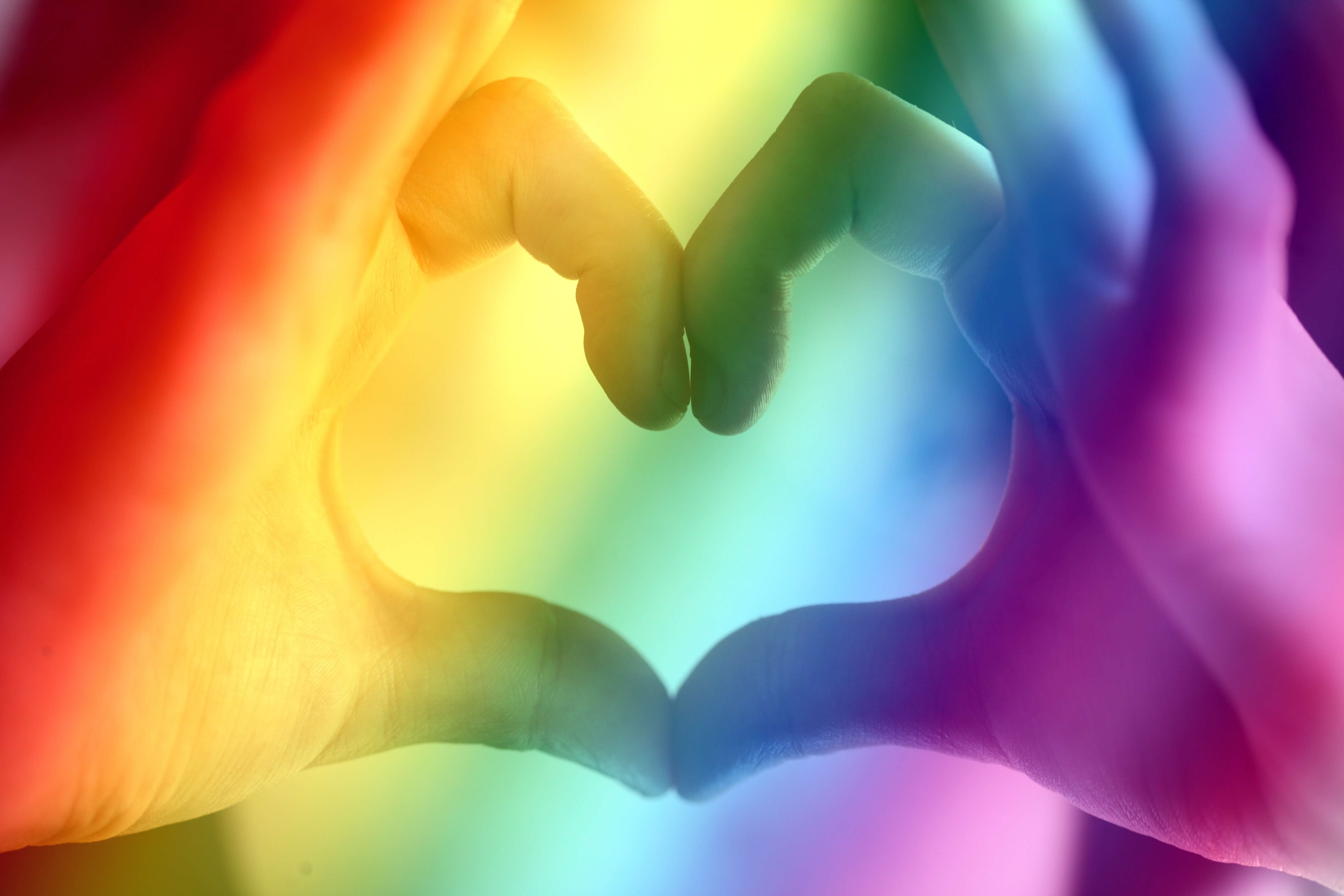 Hands shaping heart with a rainbow background color